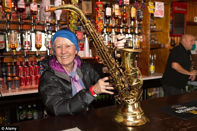 A customer poses while pulling a pint from a saxophone-decorated tap behind the bar of the Globe Tavern