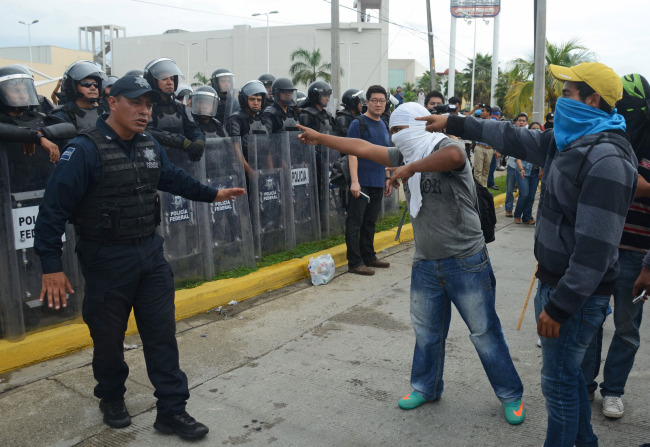 Masked students confront federal police outside the Acapulco airport as they protest the disappearance, and probable murder, of 43 students in the state of Guerrero, Mexico, Monday, Nov. 10, 2014. Relatives and supporters battled federal police in Acapulco, then blocked roads leading to the Pacific resorts airport, forcing tourists to walk to the terminal. The 43 teachers-school students disappeared at the hands of a city police force on Sept. 26 in the town of Iguala. (AP Photo/Bernardino Hernandez)