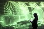An employee of the Science Museum stands in front of a video projection showing the workings of the Large Hadron Collider (LHC)  at the 'Collider' exhibition